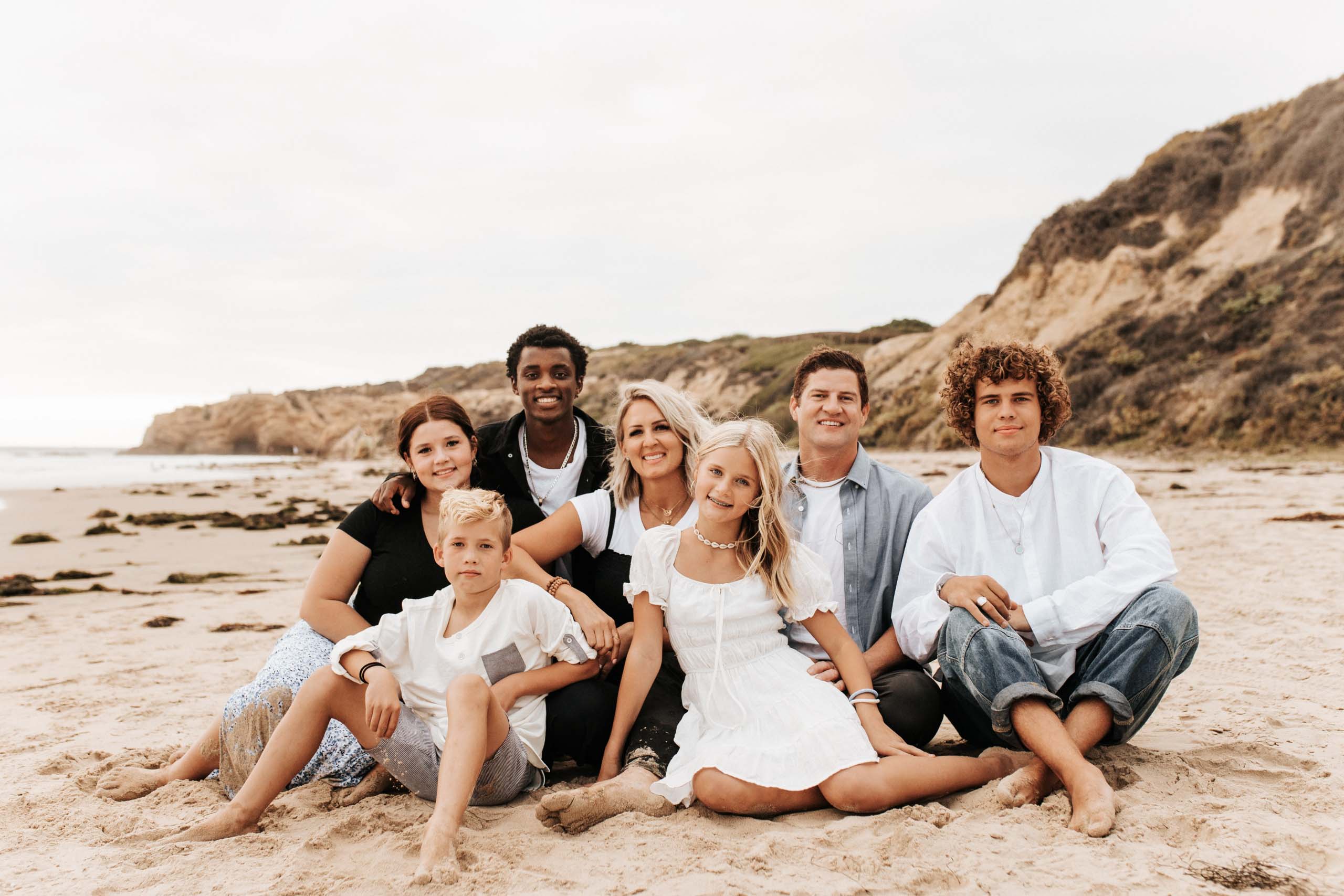 Burke family photo on a beach with ocean and cliffs in background.